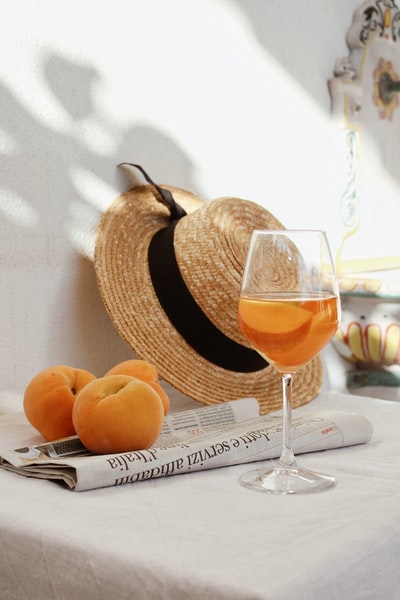 橙色水果放在透明酒杯旁的棕色编织篮子里
